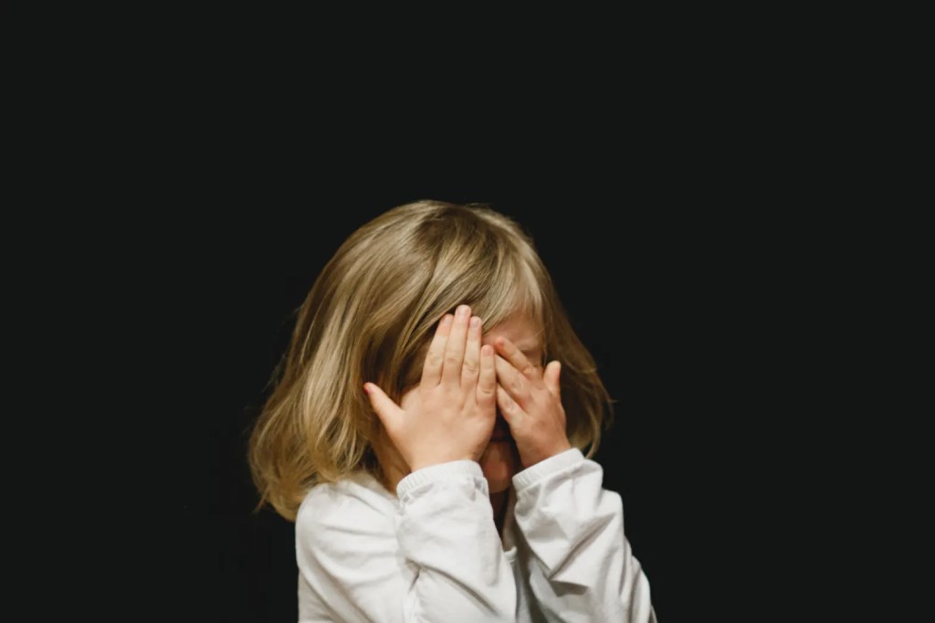 Little girl hiding her face at the fear of perception overbearing her.
